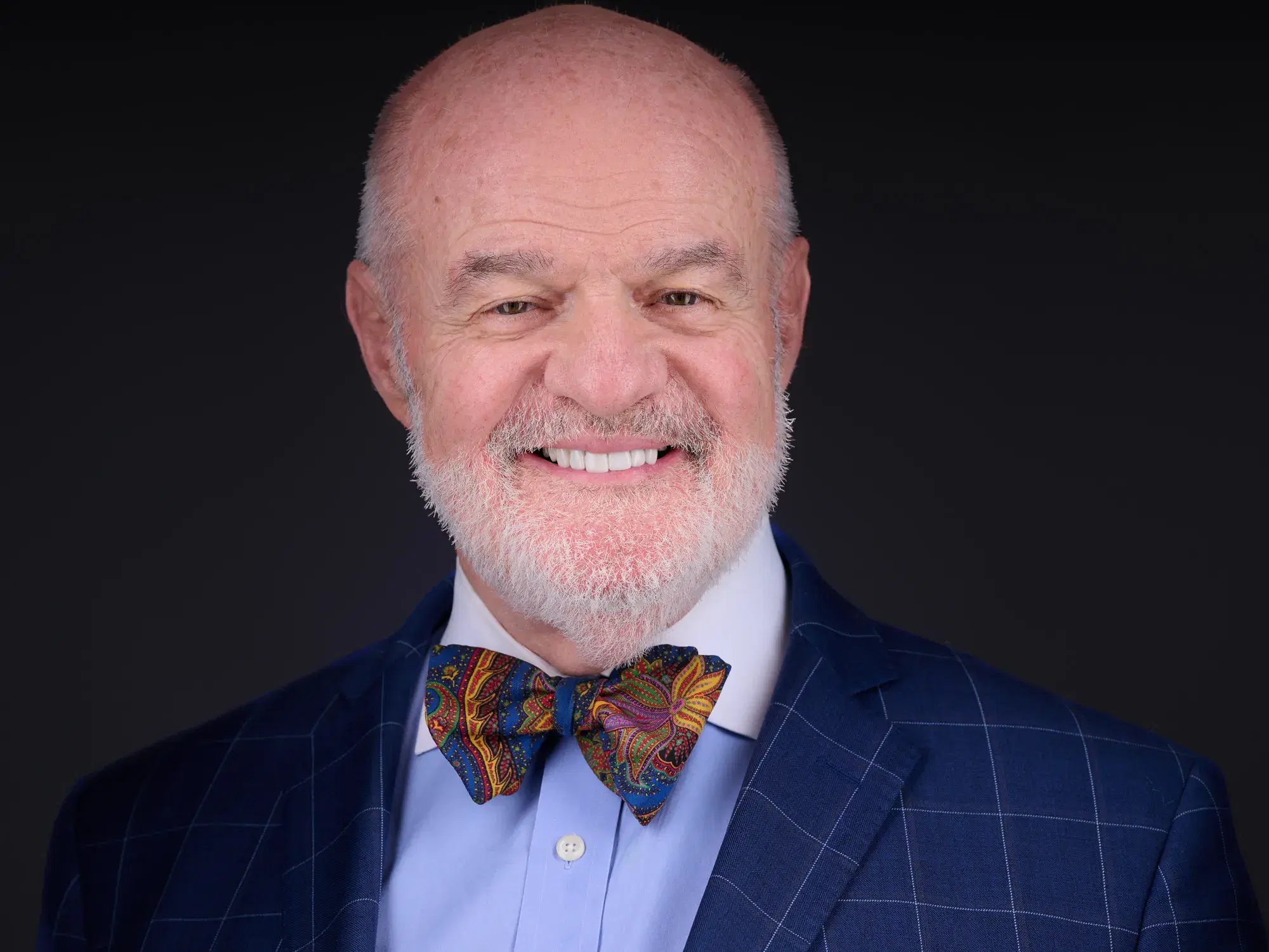 Professional headshot of warm engaging man in navy blazer and colorful paisley bow tie against neutral gray studio backdrop — Boston team headshots by Damon Bates Photography