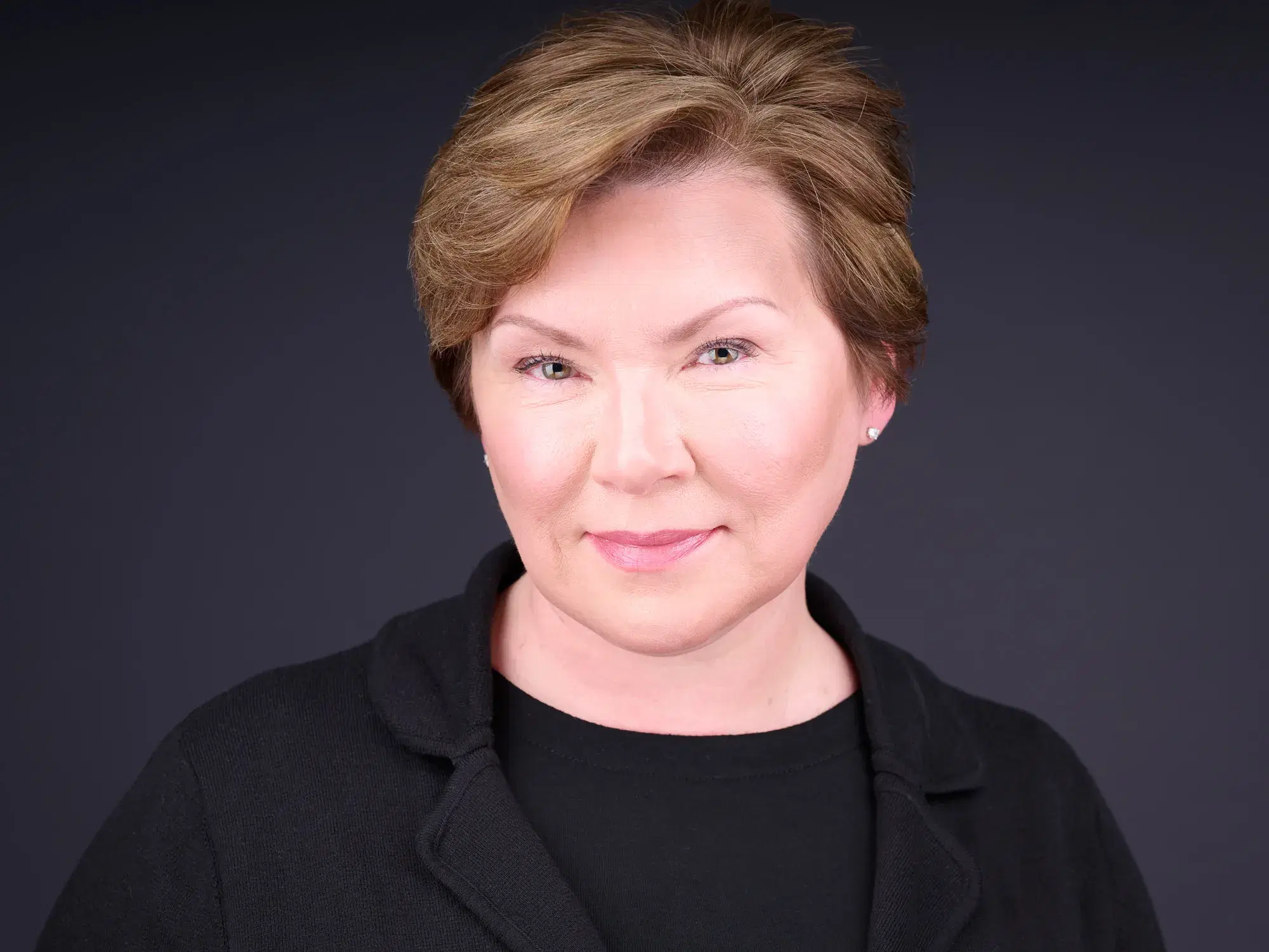 Professional headshot of composed woman with auburn hair in black top against neutral gray studio backdrop — Boston team headshots by Damon Bates Photography