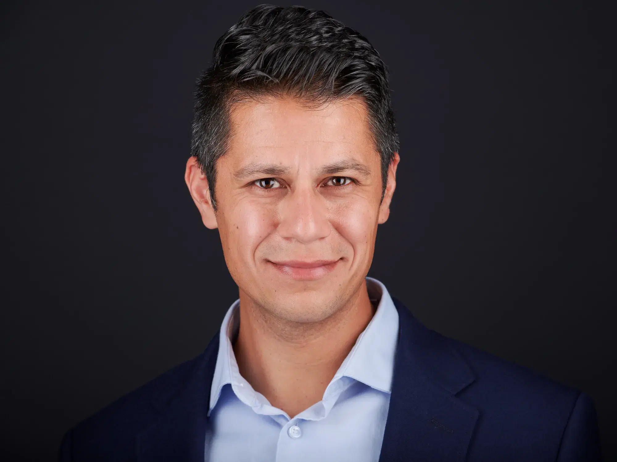 Professional headshot of approachable man in navy blazer and light blue shirt against neutral gray studio backdrop — Boston team headshot photographer Damon Bates Photography