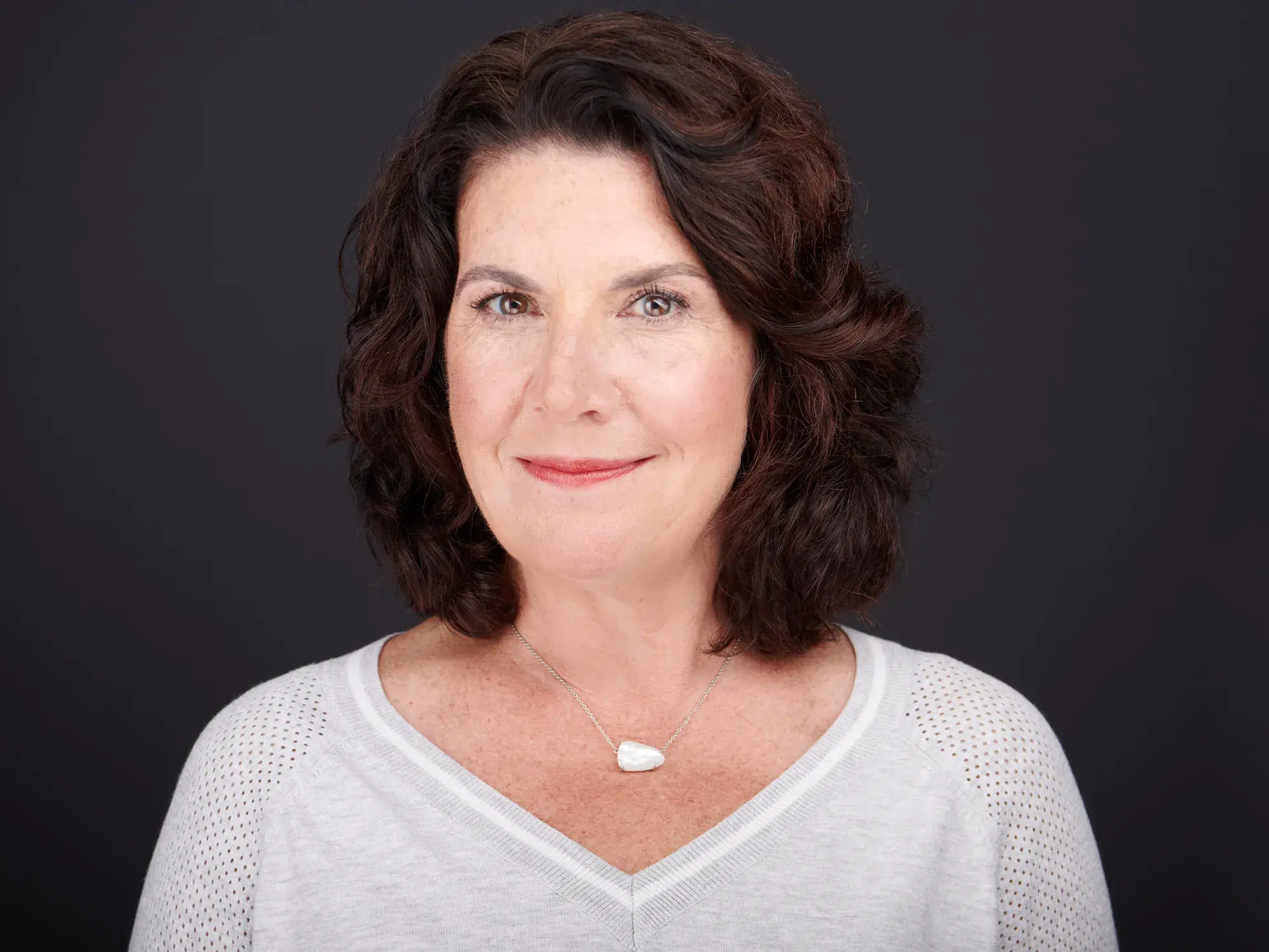 Professional headshot of confident woman in light gray sweater against neutral gray studio backdrop — Boston team headshot photographer Damon Bates Photography