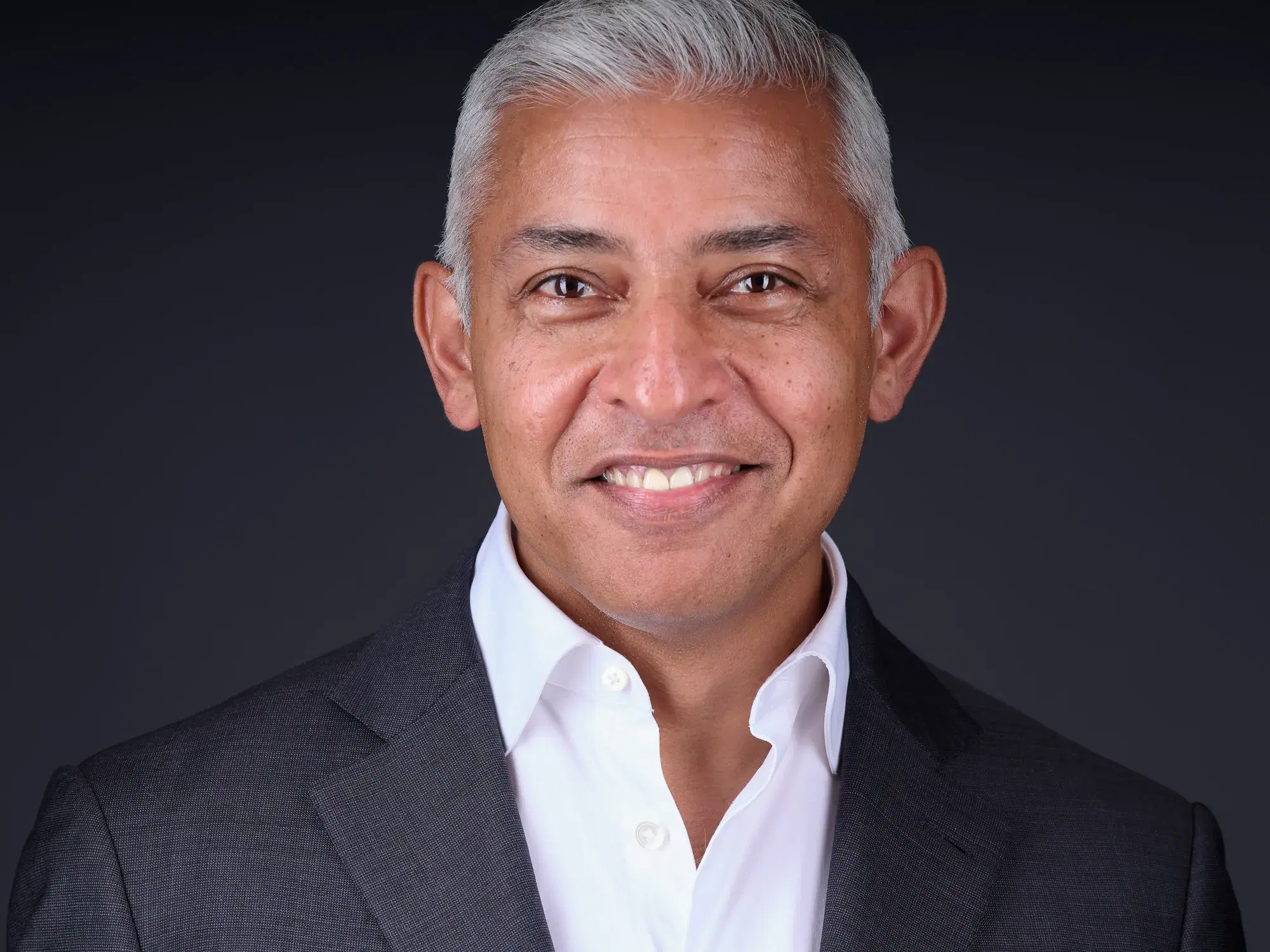 Professional male executive in pink button-down shirt with warm genuine smile against neutral gray studio backdrop — Boston executive headshot photographer Damon Bates Photography