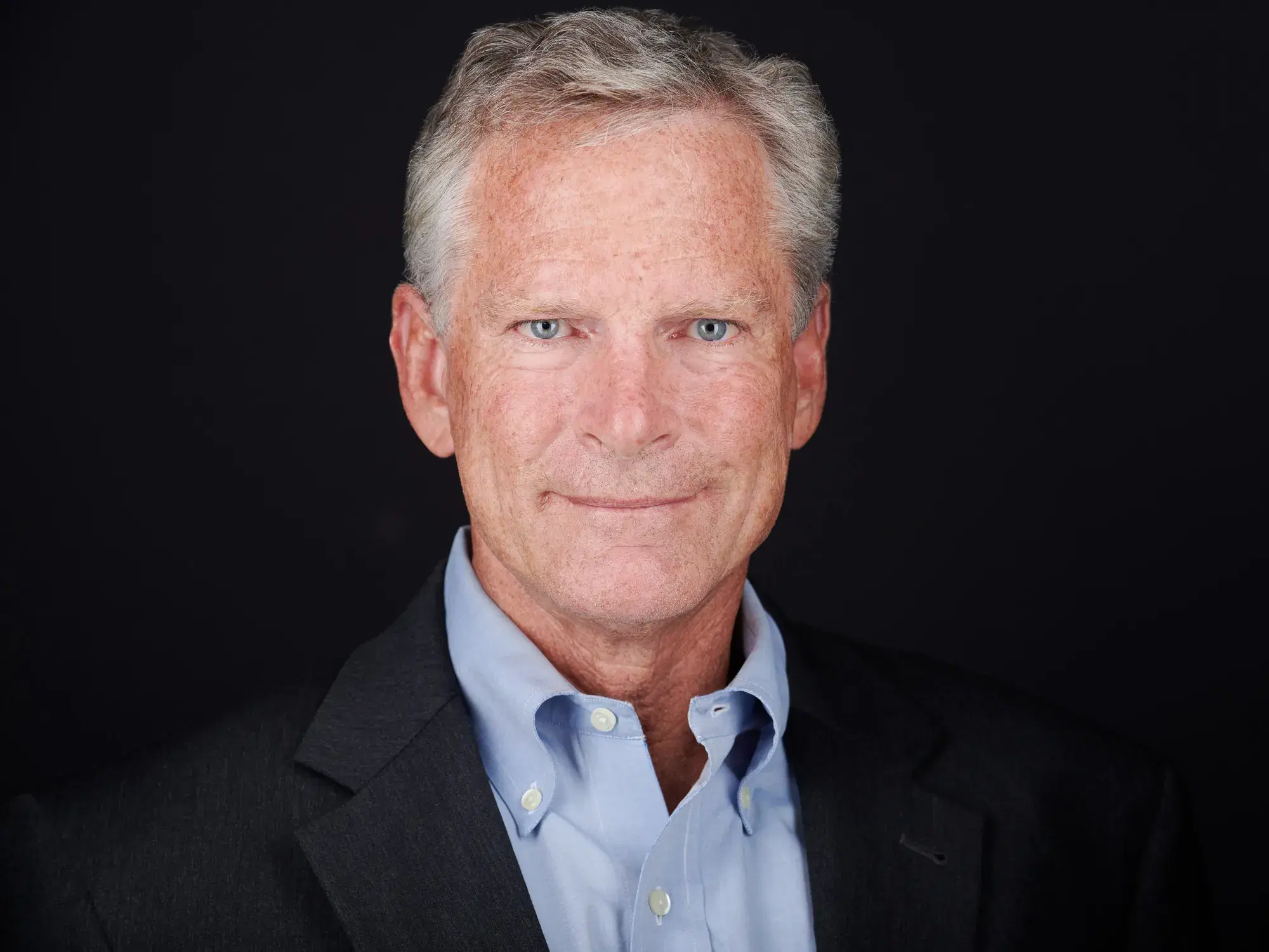 Mature male professional in business casual light blue shirt with composed confident smile against gray studio background — Boston headshot photographer Damon Bates Photography