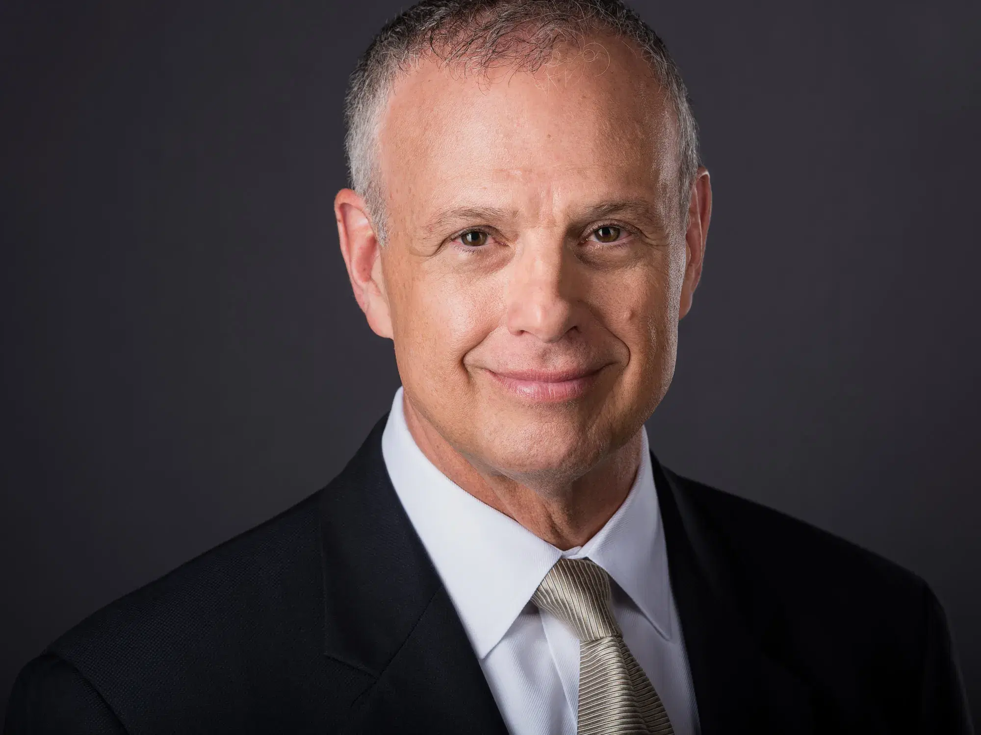 Mature male executive in black blazer and striped tie with confident smile against neutral gray studio backdrop — Boston executive headshot photographer Damon Bates Photography