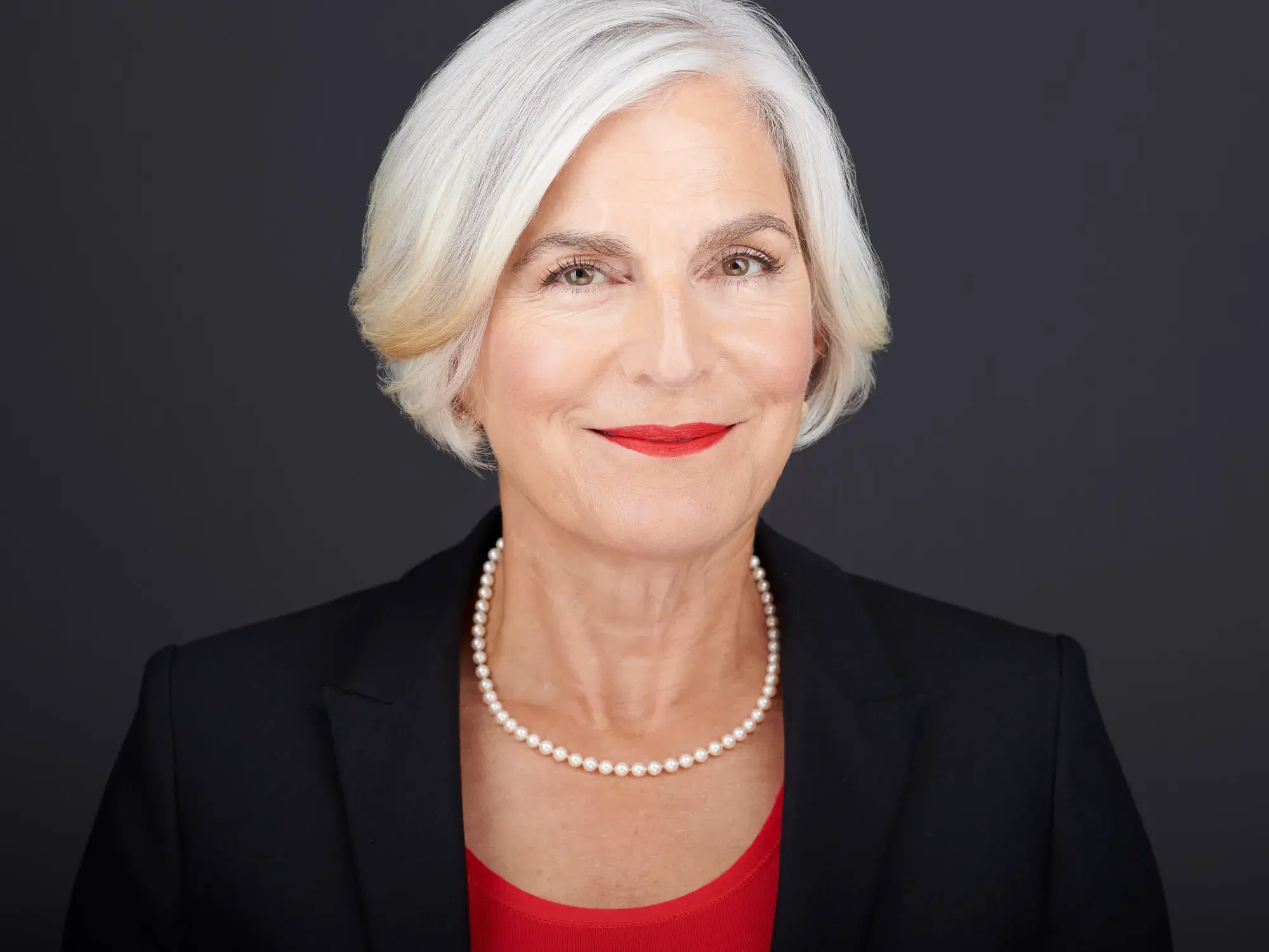 Professional studio headshot of woman in black blazer and red top with pearl necklace against dark gray backdrop — Boston headshot photographer Damon Bates Photography